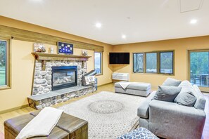 A living room with a stone fireplace, a flat-screen TV, a grey sofa, and a patterned rug. - 6,000-Sq-Ft Estate in Delaware River Valley (Milford)