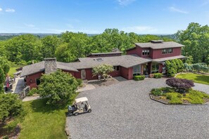 A two-story house with a stone chimney, a covered patio, and a gravel driveway. - 6,000-Sq-Ft Estate in Delaware River Valley (Milford)