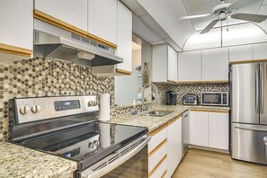 Une cuisine équipée d’une cuisinière, d’un four à micro-ondes et d’un réfrigérateur en acier inoxydable, d’un ventilateur de plafond et d’un pare-feu décoratif.