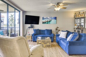 A living room with a blue sofa set, a flat-screen TV, and a ceiling fan. - 1 Block to Beach! Indian Shores Condo, Pool Access (Indian Shores)