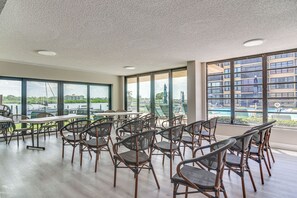 A spacious indoor area with multiple tables and chairs, large windows offering views of a body of water and buildings, and a ceiling with recessed lighting. - 1 Block to Beach! Indian Shores Condo, Pool Access (Indian Shores)
