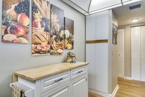 Un coin cuisine doté d’un plan de travail en bois, de meubles blancs et d’un présentoir mural pour les fruits et légumes.