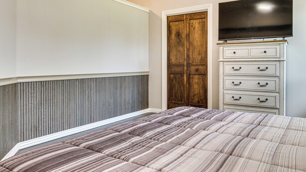 Une chambre à coucher avec un lit, une commode, un téléviseur et une porte en bois.