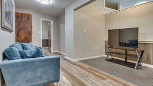 Un salon moderne avec un canapé bleu, un plancher en bois, un téléviseur posé sur un meuble et une porte donnant sur une autre pièce.