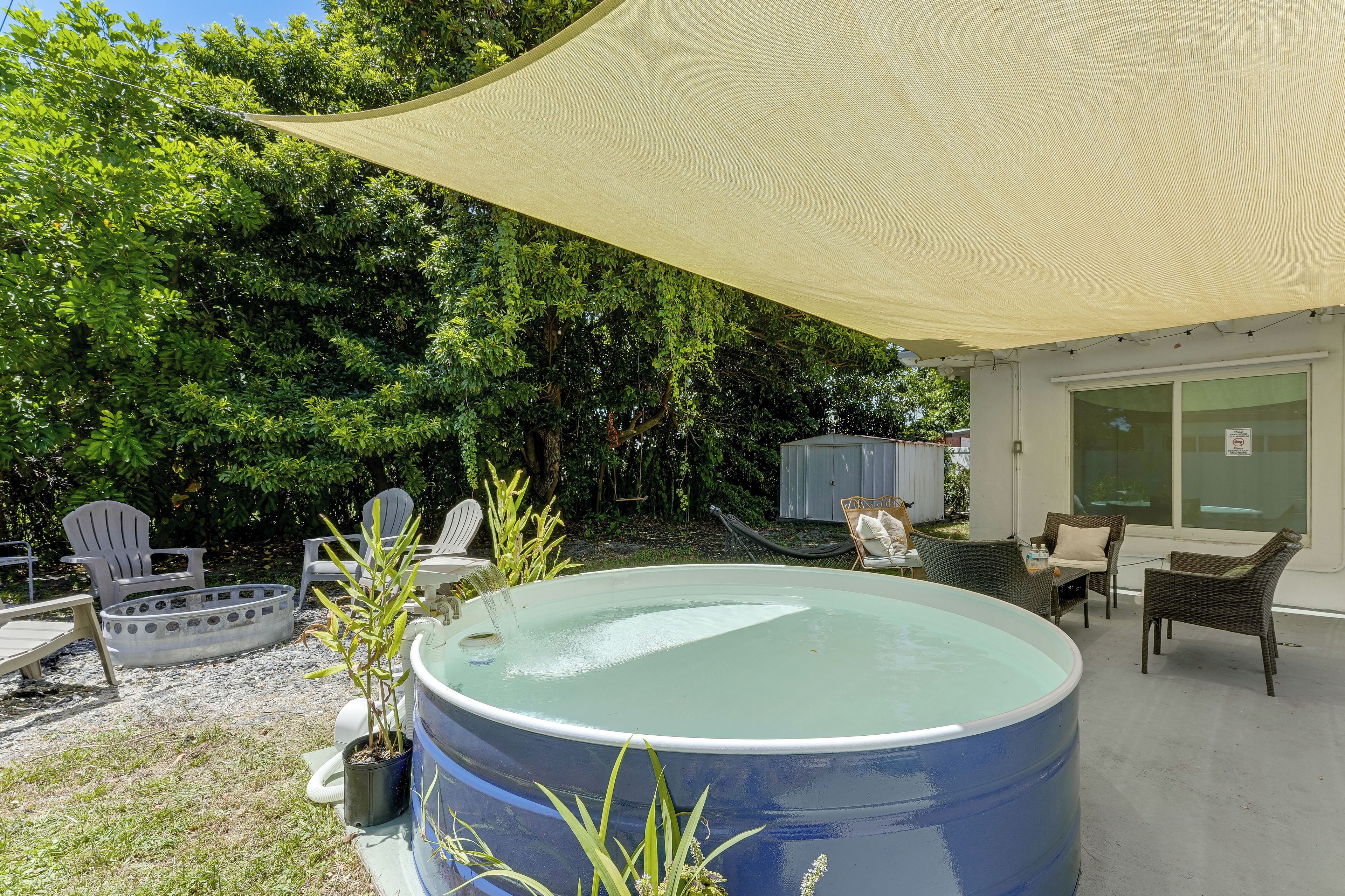 A pool area with a large blue pool, surrounded by outdoor furniture, including chairs and a table.
