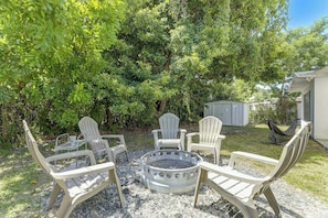 A backyard with a fire pit and four Adirondack chairs.