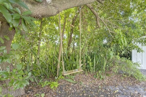 A wooden swing hanging from a tree in a lush garden area.
