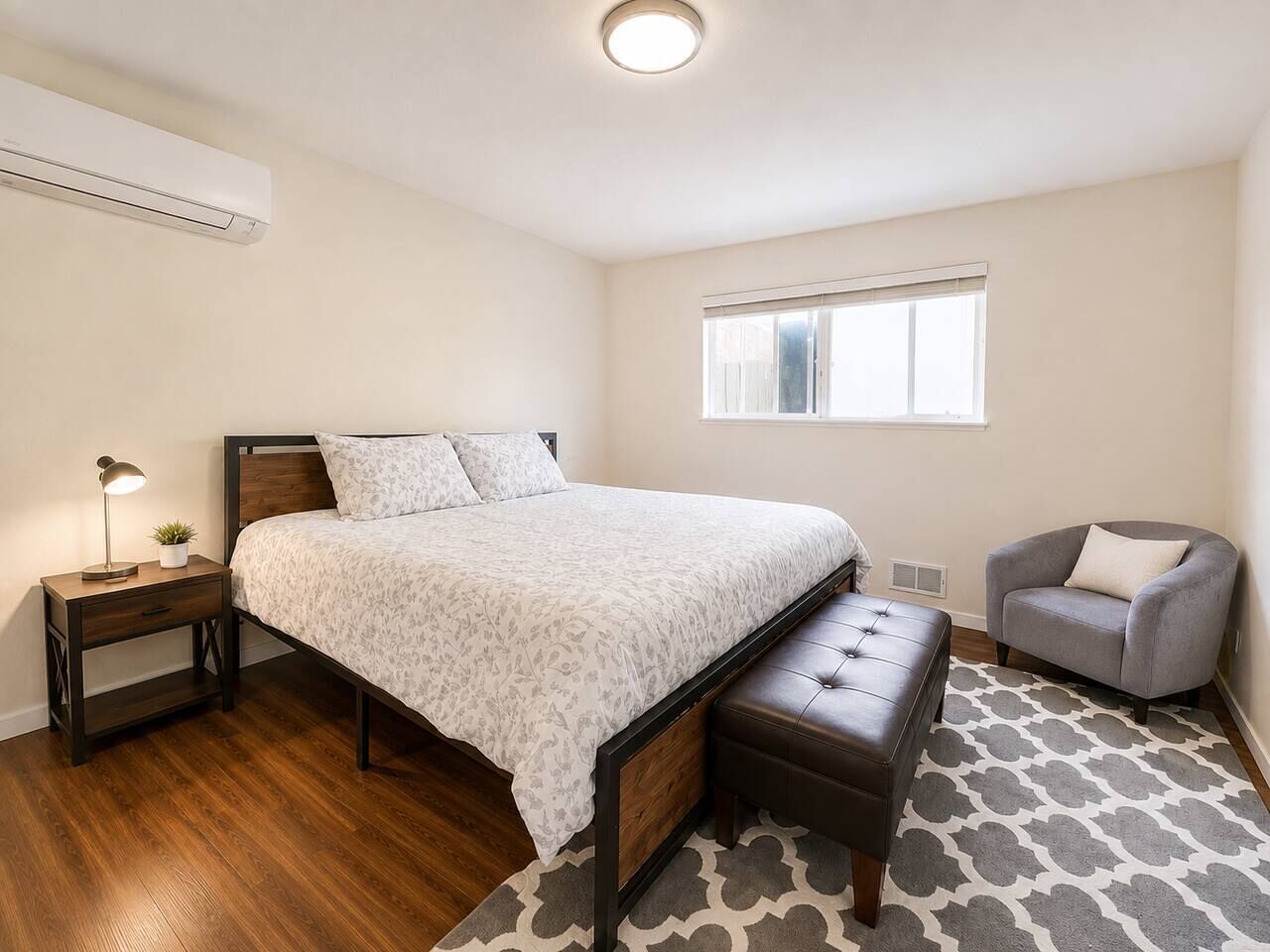 A bedroom with a bed, bedside table, lamp, chair, and a window.