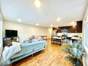 A modern living room with a sofa, a television, and a kitchen area with cabinets and appliances. - Modern 2BR/2BA in Queen Anne | Near Seattle Center / Seattle Downtown (Seattle)