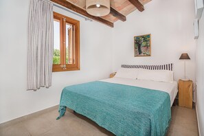 A bedroom with a bed, a window with curtains, a painting on the wall, and a bedside lamp. - Romantic Country Hideaway in Pollensa (Pollença)