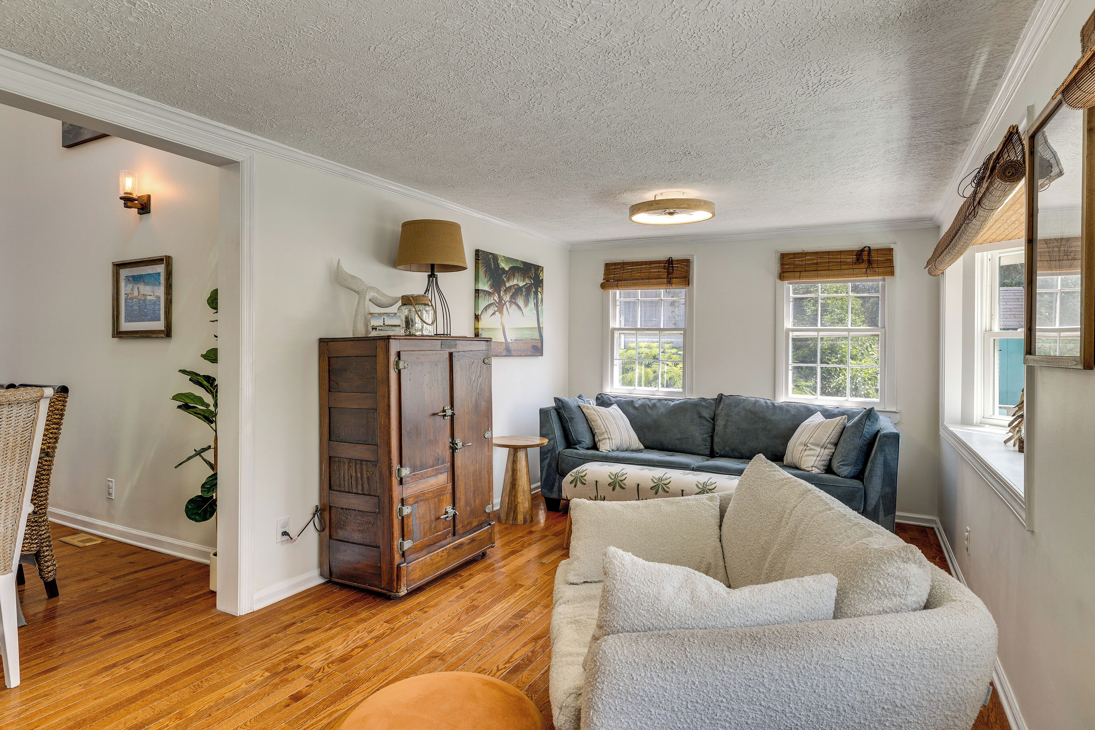 A living room with a wooden floor, a blue sofa, a wooden cabinet, and a window with a view of greenery.
