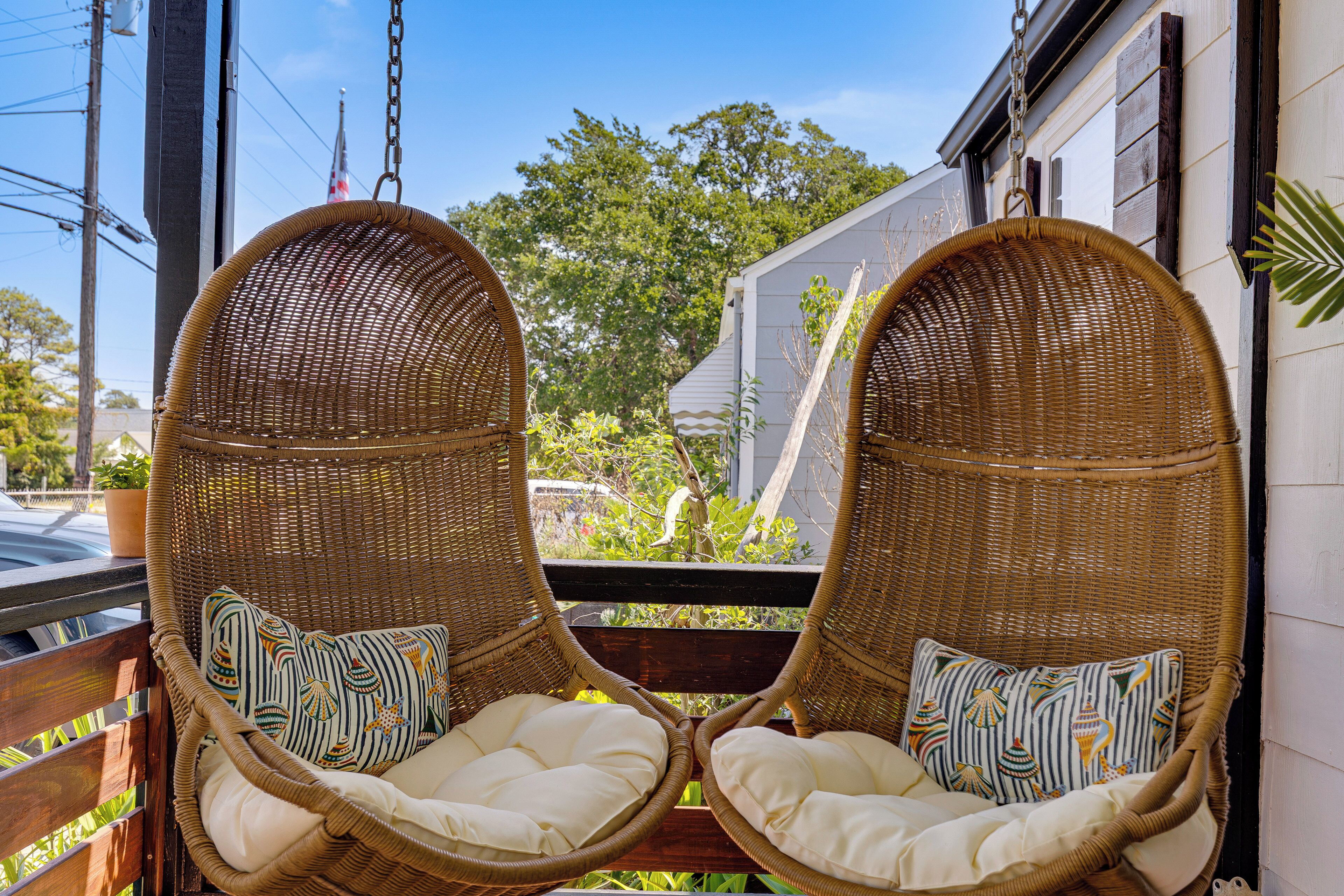 Two wicker chairs with cushions on a balcony with a view of trees and a building.