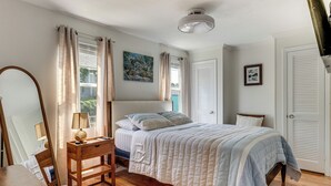 Een slaapkamer met een bed, nachtkastje, lamp, raam met gordijnen, plafondlamp en een deur.