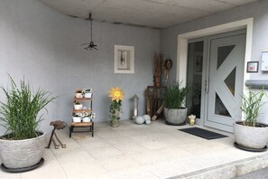 A front porch with potted plants, a small shelf with decorative items, and a door with a geometric design. - Holiday apartment with 1 bedroom (Gaschurn)