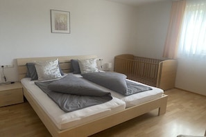 A bedroom with a bed, a crib, a nightstand, and a wall-mounted light. - Holiday apartment with 1 bedroom (Gaschurn)
