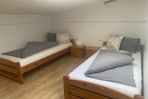 Une chambre avec deux lits en bois, chacun muni d’un oreiller gris et d’une table de chevet avec une lampe.