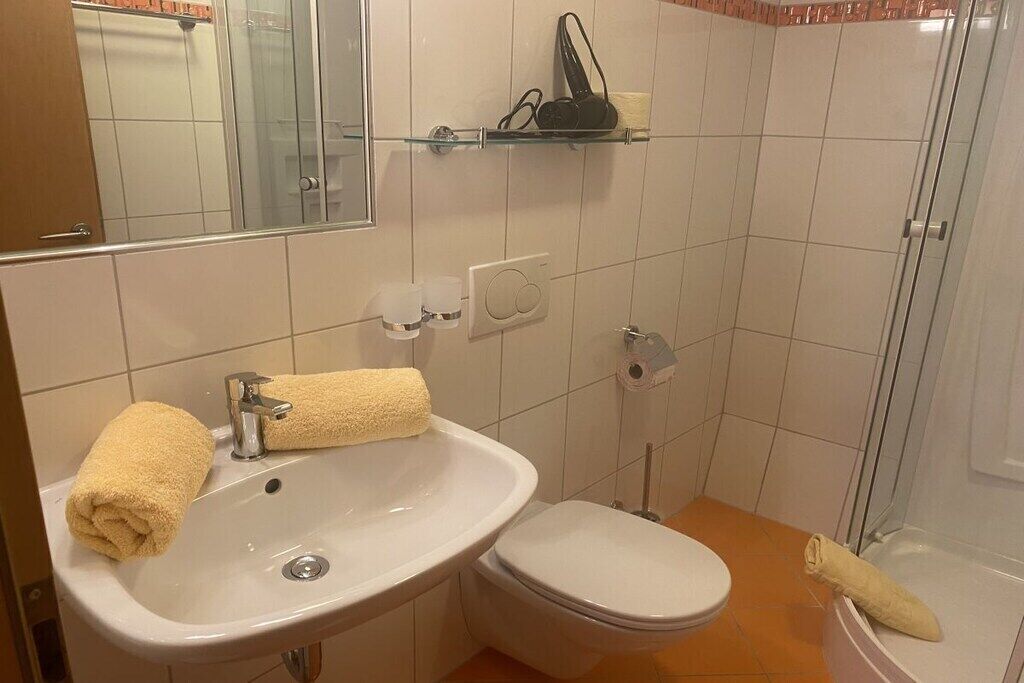 Kylpyhuone, jossa on valkoinen pesuallas, wc-istuin ja lasinen suihkuseinä.