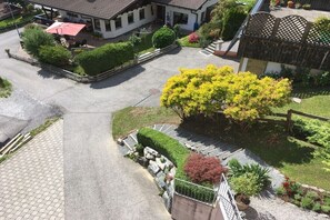 A residential property with a paved driveway, a covered outdoor seating area, and a well-maintained garden with various plants and a large yellow flowering tree. - Holiday apartment with 1 bedroom (Gaschurn)
