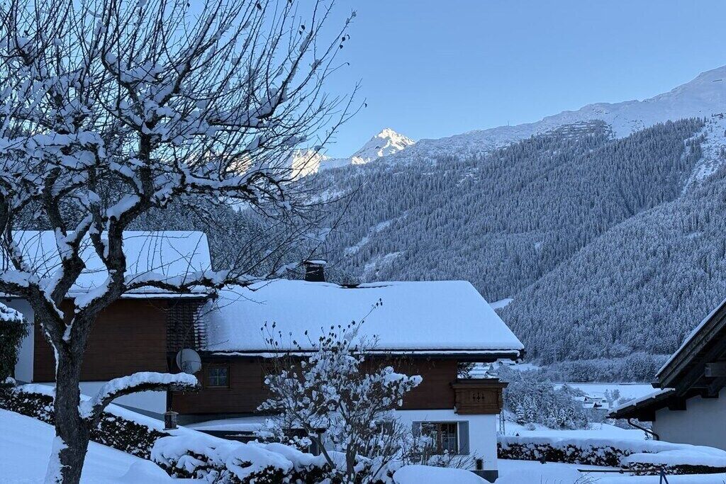 Un paysage de montagne enneigé, avec une maison au premier plan.