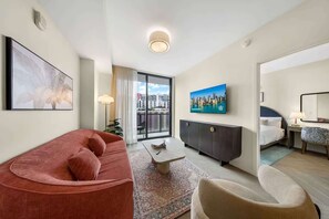 A modern hotel room with a red sofa, a small coffee table, a grey cabinet, a TV on the wall, and a balcony with a city view. - Wynwood Miami | NoMad 1BR + Rooftop Pool (Miami)