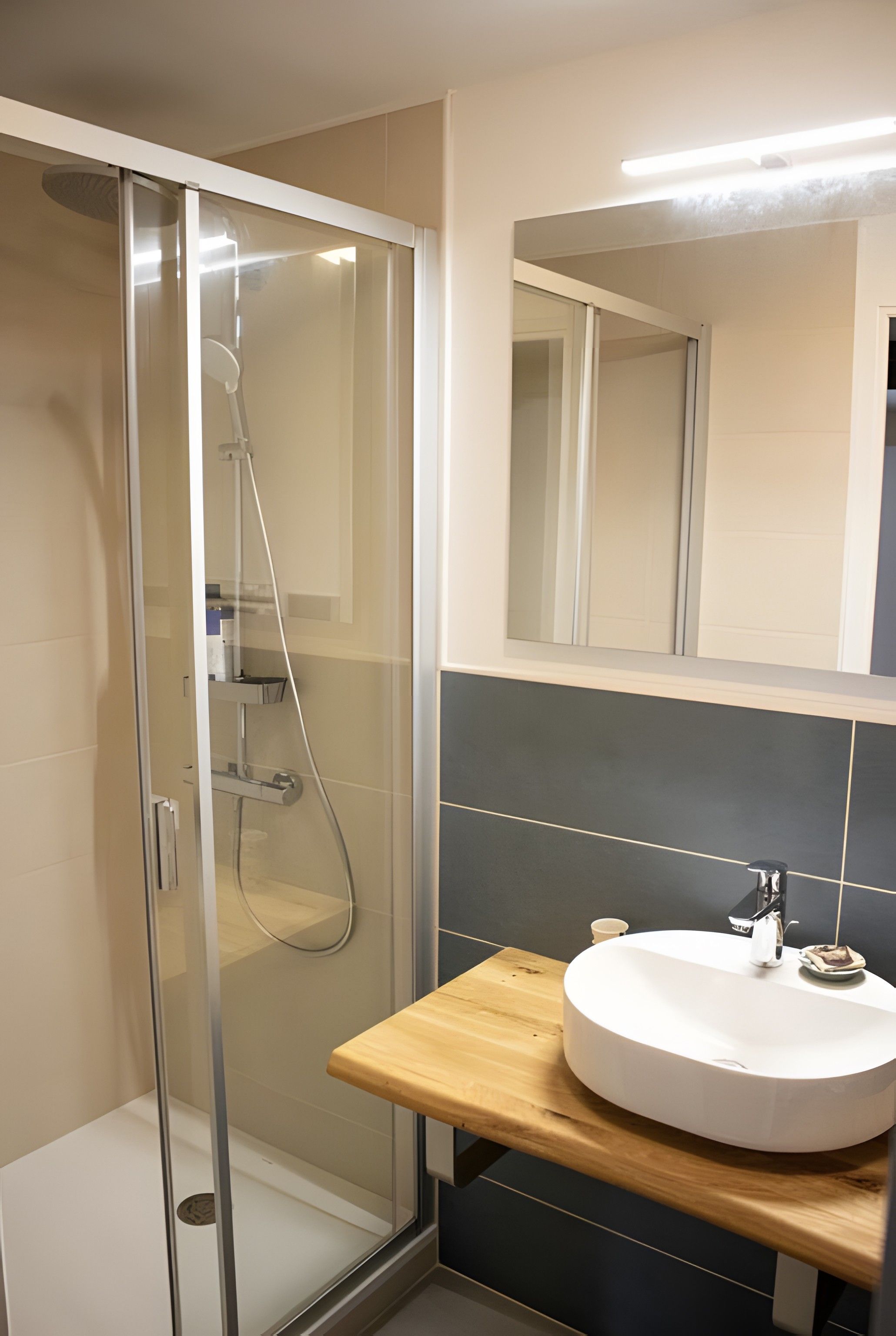 A modern bathroom with a glass-enclosed shower, a wooden vanity with a white sink, and a mirror above the sink.