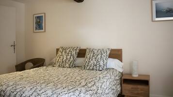 Une chambre à coucher avec un lit, deux oreillers, une table de chevet, une chaise et une porte.