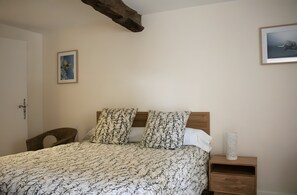 Een slaapkamer met een bed, twee kussens, een nachtkastje, een stoel en een deur.