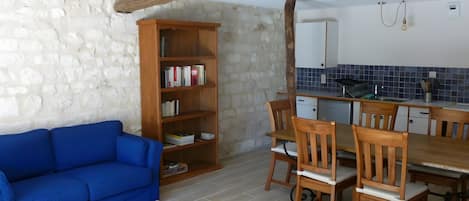 Ein Zimmer mit einem blauen Sofa, einem Holzespeisebereich mit Stühlen, einem Bücherregal und einer Küchenzeile mit blauen Fliesen.