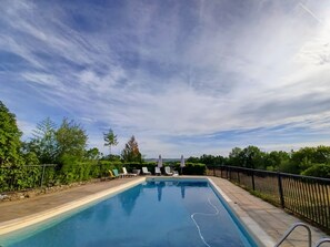 Una piscina con sillones de descanso y vistas al cielo.