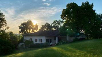 Une maison avec un toit en pente, entourée d’une pelouse et d’arbres.