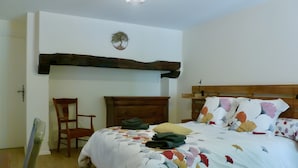 Un dormitori amb un capçal de llit de fusta, un llit amb un edredó floral, una nitzeta de fusta i una cadira.