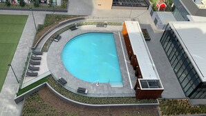 Ein Schwimmbecken mit geschwungener Kante, umgeben von einem Gehweg mit Sitzbereichen.