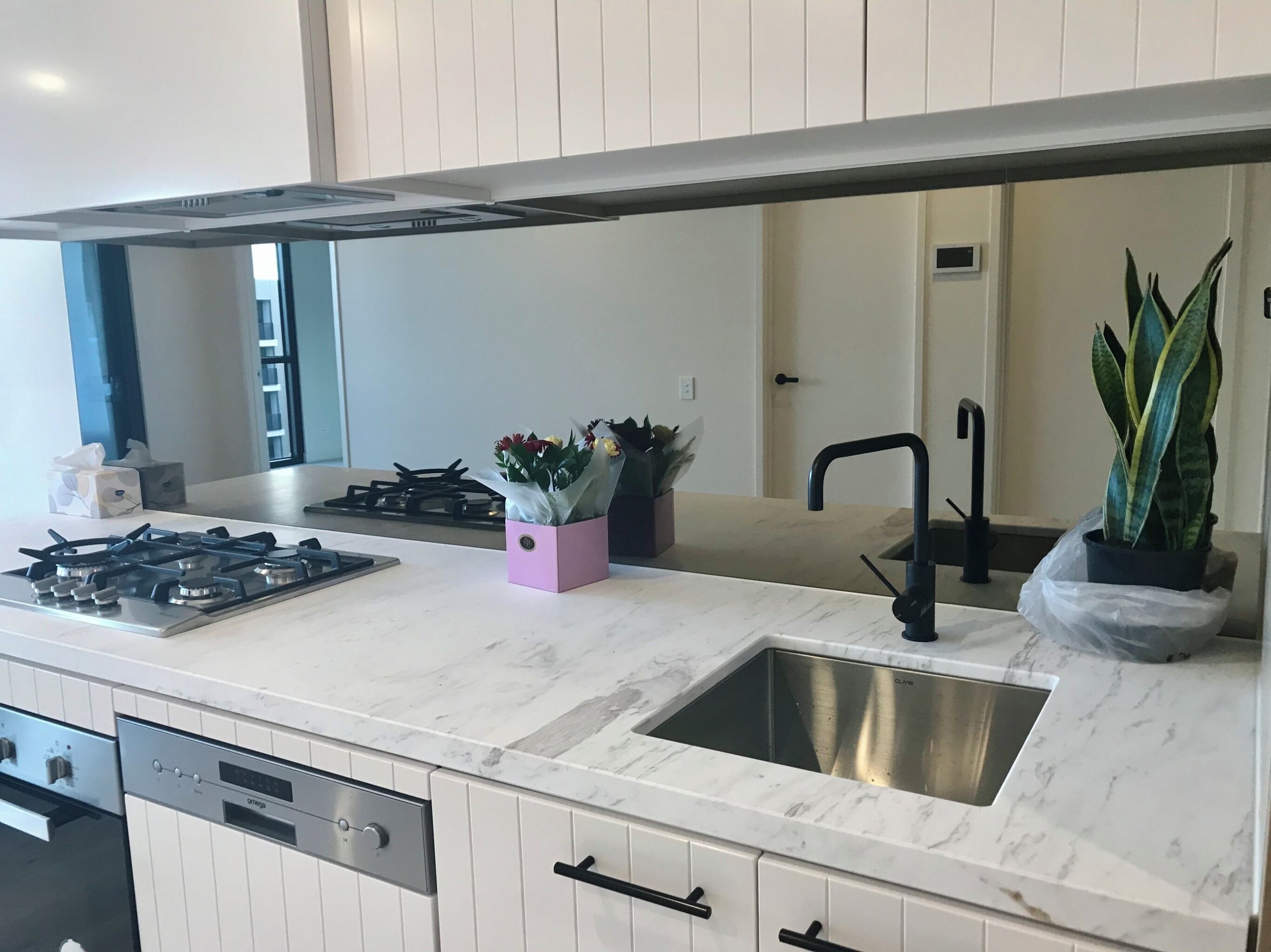 A modern kitchen with a gas stove, stainless steel sink, and white cabinetry.