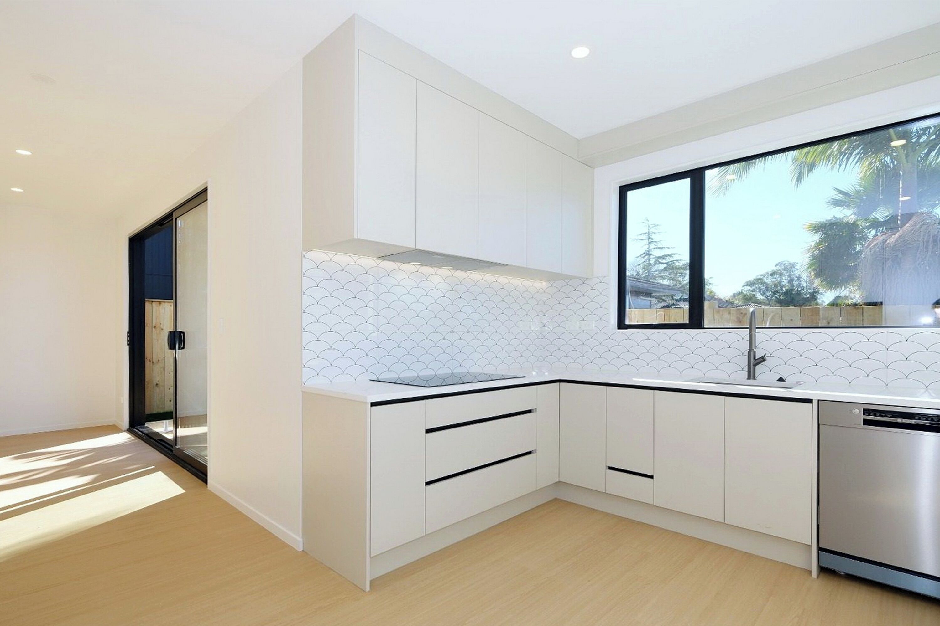 A modern kitchen with white cabinetry, a tiled backsplash, and a large window.