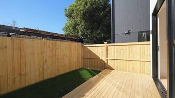 A wooden deck with a small grassy area, a wooden fence, and a building with a metal exterior.