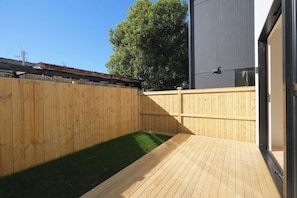 A wooden deck with a small grassy area, a wooden fence, and a building with a metal exterior.