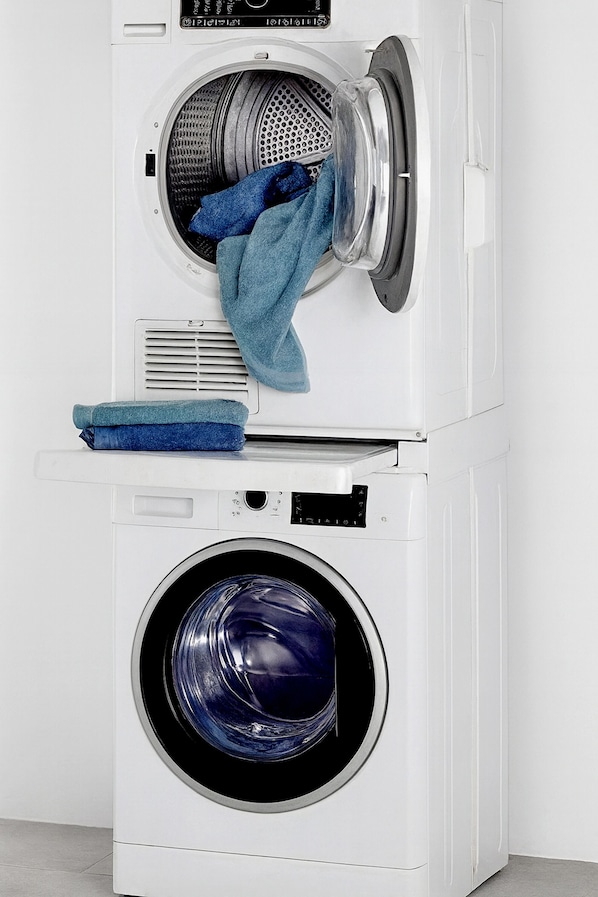 A stacked washer and dryer unit with a blue towel on the top dryer and a blue plastic basin on the bottom dryer.