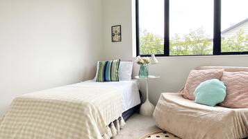 A bedroom with a bed, a chair, a small table with a lamp, and a window with a view of trees.