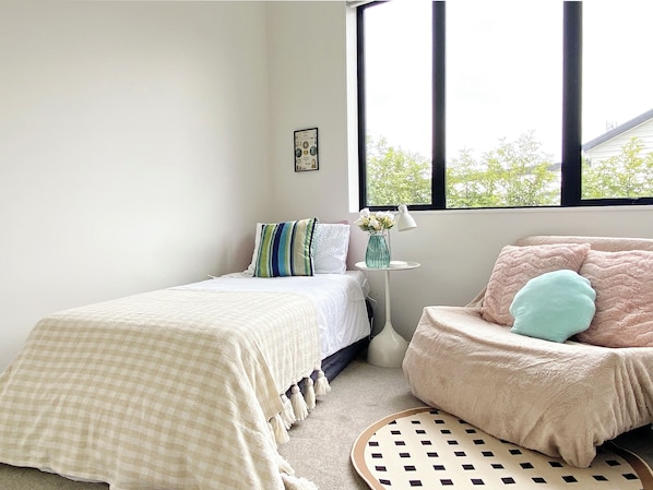 A bedroom with a bed, a chair, a small table with a lamp, and a window with a view of trees.