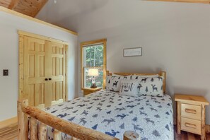 A bedroom with a wooden bed frame, a window with a view of trees, and a sign on the wall. - Dahlonega Wine Country Cabin w/ Hot Tub! (Dahlonega)