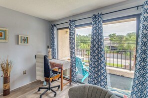 Quarto com escrivaninha, cadeira de escritório e vista para o exterior.
