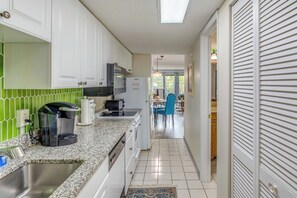 Cozinha com armários brancos, bancada de granito, cafeteira e área de jantar com mesa e cadeiras.