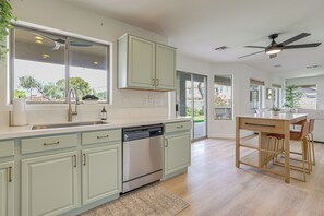 A modern kitchen with a dishwasher, a dining area with a table and chairs, and a ceiling fan. - Golf View, Pool Access! Updated Queen Creek Home (Queen Creek)