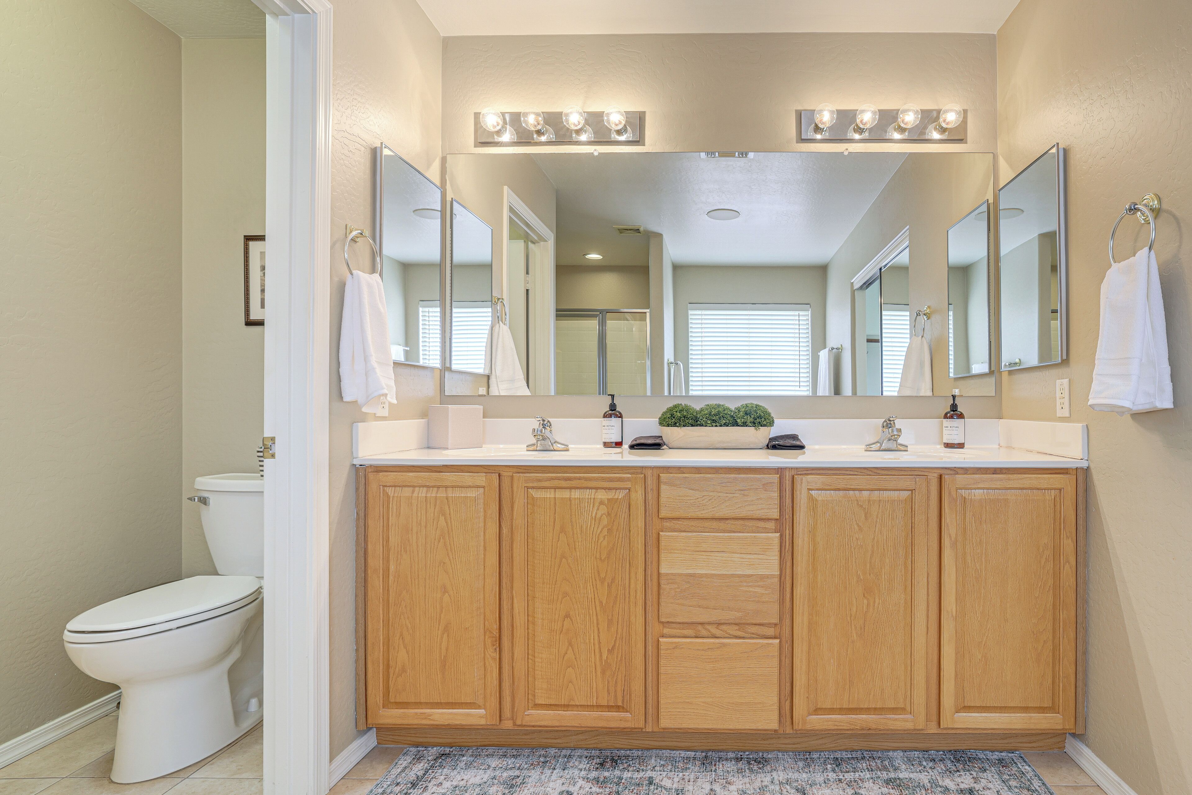 A bathroom with wooden cabinets, a white sink, and a large mirror with lights above.