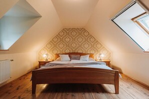 A bedroom with a sloped ceiling, a wooden bed, patterned wallpaper, and two bedside lamps. - Holiday apartment with 1 bedroom (St. Johann)
