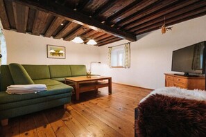 Una sala de estar acogedora con un sofá verde, una mesa de centro de madera, un televisor y un plaid de piel.
