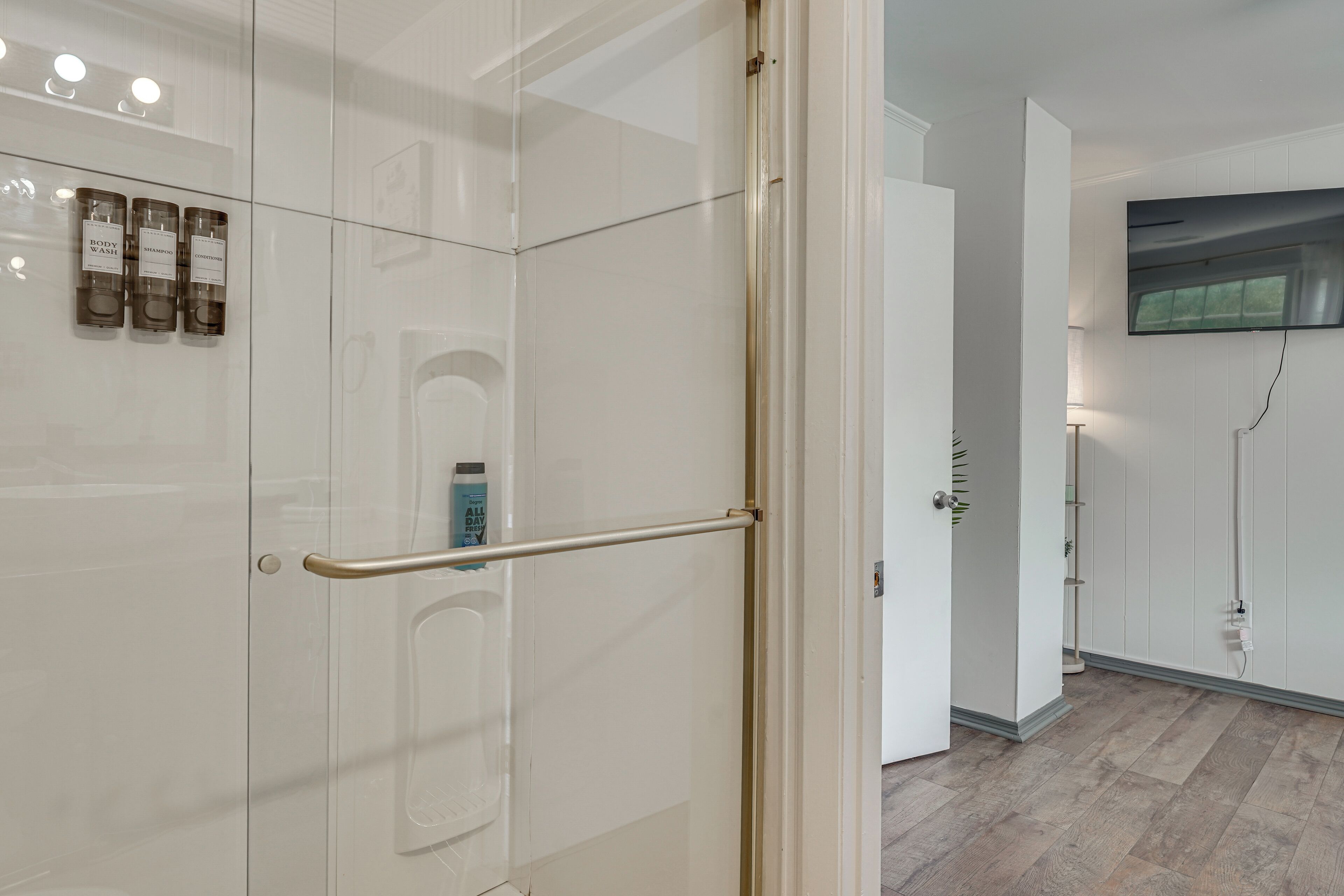 Une salle de bain moderne avec une douche à parois de verre, une barre d’appui et un téléviseur fixé au mur.