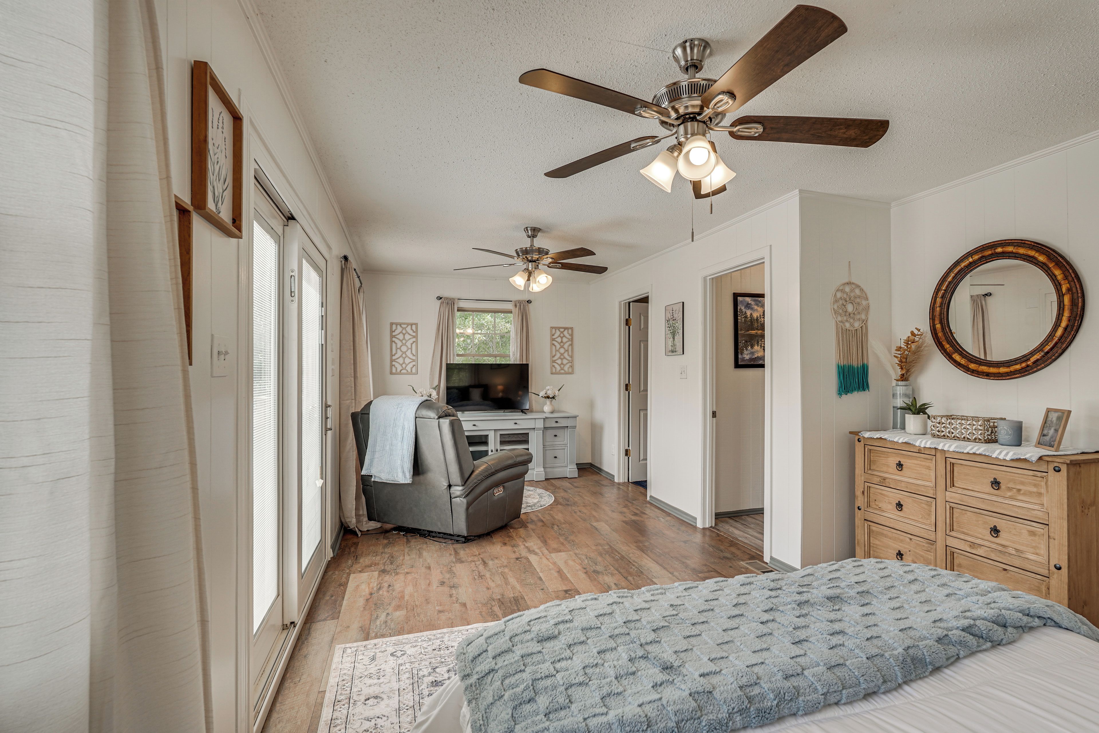 A bedroom with a bed, a dresser, a ceiling fan, and a television in the background.