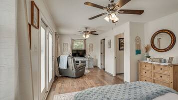 A bedroom with a bed, a dresser, a ceiling fan, and a television in the background.