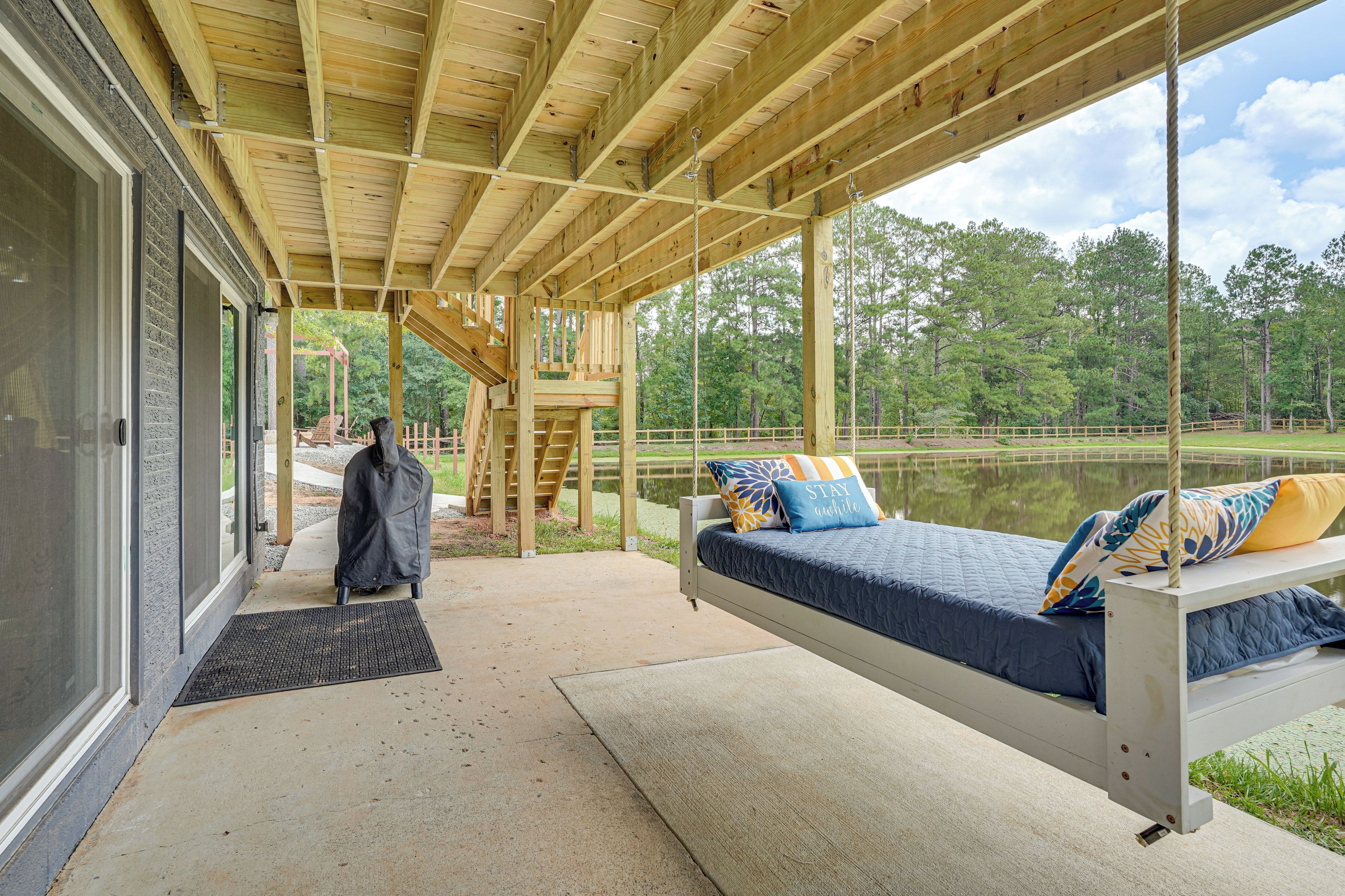 A covered outdoor seating area with a bed, a bench, and a view of a lake.